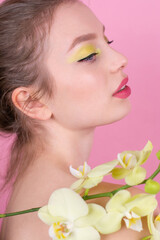 Young woman with spring make up close eyes holding orchid flowers isolated on pink background Close up Beauty Cosmetics concept