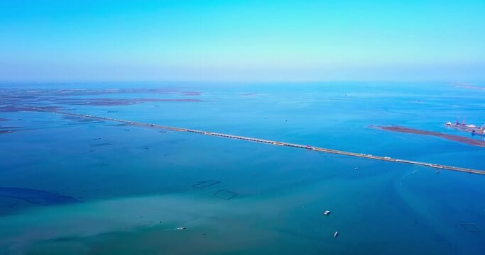 Endless bright blue lagoon panorama with transparent water crossed by road on narrow ground polder strip on sunny day aerial view