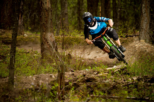 A mountain biker  a downhill bike on a berm through the trees.