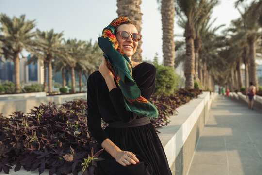 Young Woman Sitting On The Wall And Holding Her Head Scarf