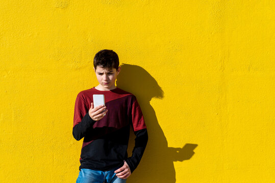 Young teen leaning against a yellow wall while using a mobile phone