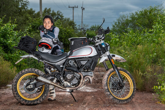 Woman Posing Behind Her Scrambler Style Motorcycle On Dirt Road