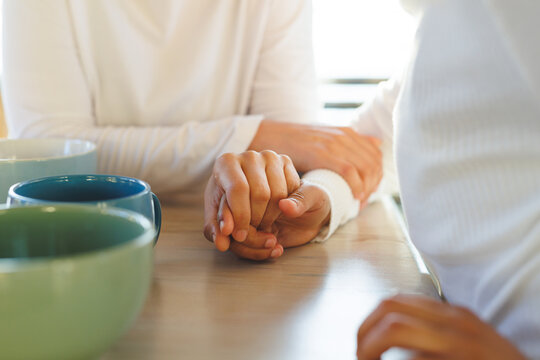 Midsection of diverse lesbian couple holding hands in kitchen - Powered by Adobe