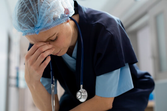 Tired caucasian female doctor wearing hair net working at hospital, sitting on floor in corridor