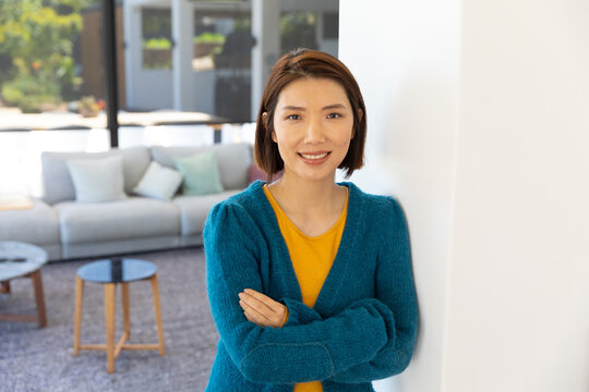 Portrait of happy asian woman standing in living room, smiling to camera, copy space