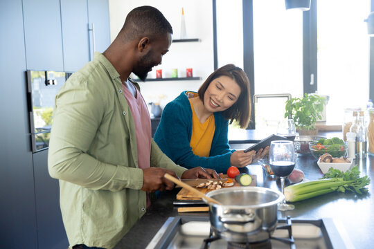 Happy diverse couple cooking together and using tablet in modern kitchen, copy space