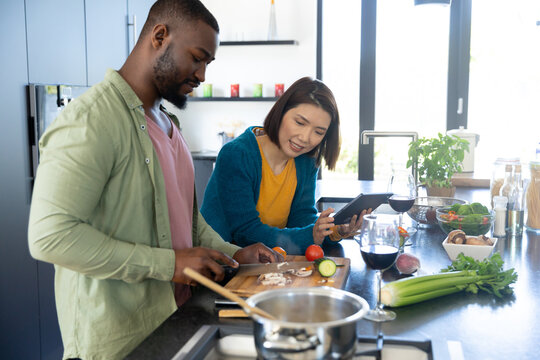 Happy diverse couple cooking together and using tablet in modern kitchen, copy space