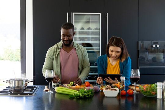 Happy diverse couple cooking together and using tablet in modern kitchen, copy space