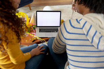 Rear view of happy biracial couple making celebration video call on laptop, copy space on screen