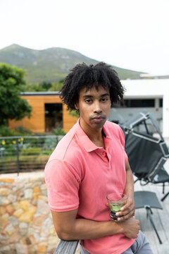 Vertical portrait of biracial man relaxing with drink on sundeck at holiday home, copy space