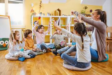 Kindergarten teacher with children sitting on the floor having music class, using various instruments and percussion. Early music education