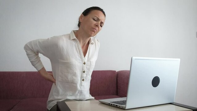 Woman With Back Fatigue With Laptop Indoor. A View Of Sad Stressed Woman Suffering From Back Pain During Her Online Typing On Computer At Home.