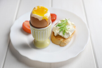 Fototapeta premium Fresh soft boiled egg in cup and sandwich on white wooden table