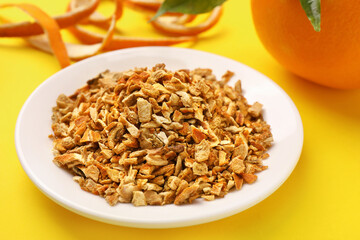 Plate with dried orange zest seasoning, fresh peel and fruit on yellow background, closeup