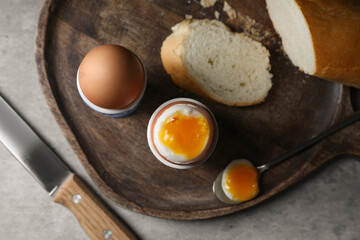 Fresh soft boiled eggs in cups and bread on grey table, flat lay