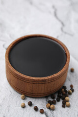 Wooden bowl with balsamic vinegar and peppercorns on white textured table, closeup