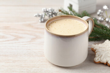 Cup of delicious eggnog and cookie on wooden table, space for text