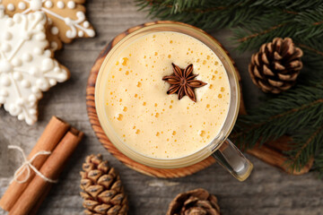 Glass of delicious eggnog with anise star on wooden table, flat lay