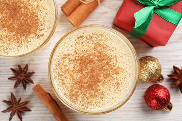 Tasty eggnog with cinnamon, anise stars and Christmas decorations on white wooden table, flat lay