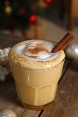 Tasty eggnog with cinnamon on wooden table against blurred festive lights, closeup