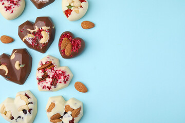 Tasty chocolate heart shaped candies with nuts on light blue background, flat lay. Space for text