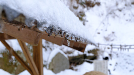 雪深い日本の山中にある小屋の屋根に積もった雪からできた氷柱