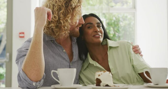 Happy diverse couple with coffee embracing and talking in cafe