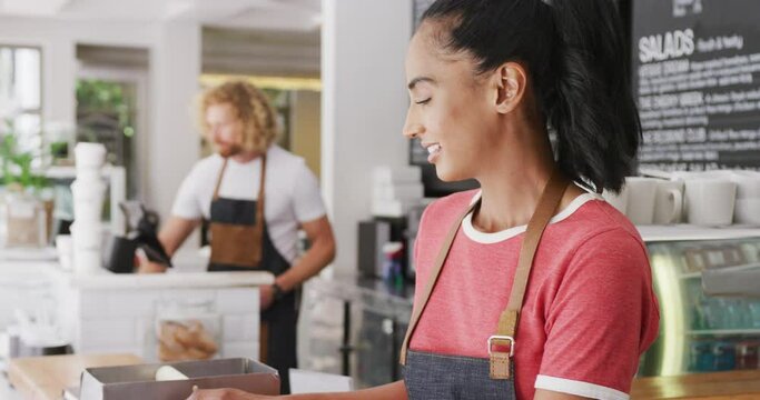 Portrait of happy biracial female barista, smiling behind the counter in cafe