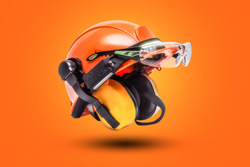 Protective goggles for eyes and construction helmet for head with earmuffs and headlamp on a orange background. Construction tool and form for protection.