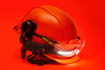 Protective goggles for eyes and construction helmet for head with earmuffs and headlamp on a red background. Construction tool and form for protection. © vadish