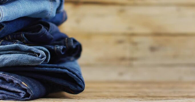 Close up of folded jeans with different shades on wooden background with copy space