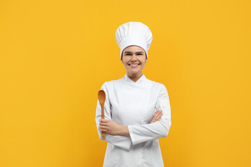 Happy female chef with wooden spoon on orange background