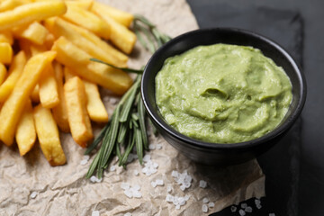 Serving board with french fries, guacamole dip and rosemary on black table, closeup