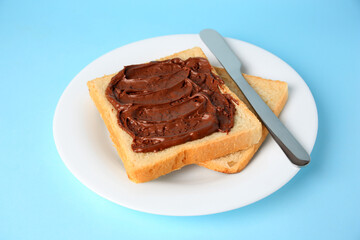 Tasty toast with chocolate paste on light blue background