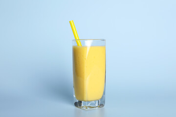 Glass of tasty smoothie with straw on light blue background