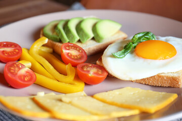 Tasty toasts with fried egg, avocado, cheese and vegetables on plate, closeup
