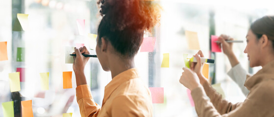 Young businesswoman creative team using post it notes in glass wall to writing strategy business...