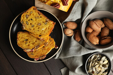 Delicious pumpkin bread with pecan nuts and seeds on wooden table, flat lay