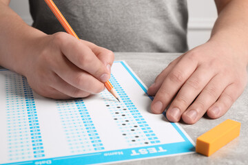 Student filling answer sheet at table, closeup. Passing exam