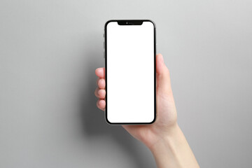 Woman holding smartphone with blank screen on grey background, closeup. Mockup for design