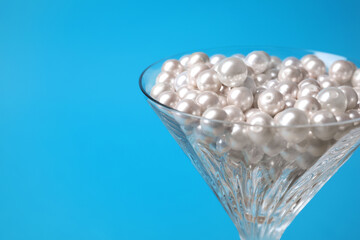 Obraz na płótnie Canvas Beautiful martini glass with pearls on light blue background, closeup. Space for text