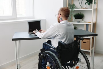 A man wheelchair businessman with tattoos in the office works at a laptop online, business process, a wheelchair close-up, integration into society, the concept of working a person with disabilities