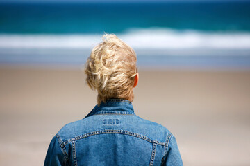 Rear view of mature woman looking out over sand beach and Ocean.