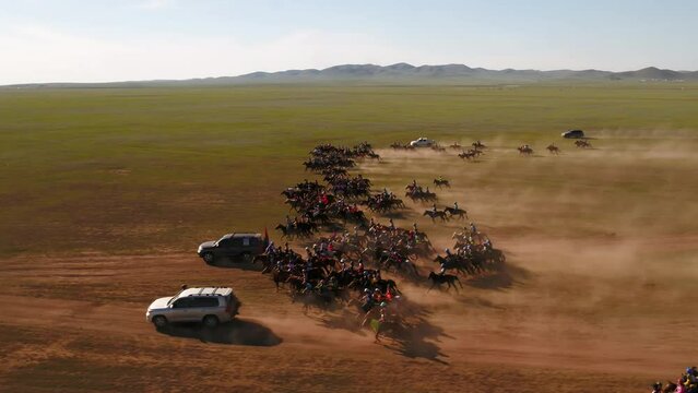 Cinematic Drone shot of a group of jockeys riding in a fast canter and gallop over the Mongolian steppe. The horseback riders are training for a traditional horserace called a Naadaam.