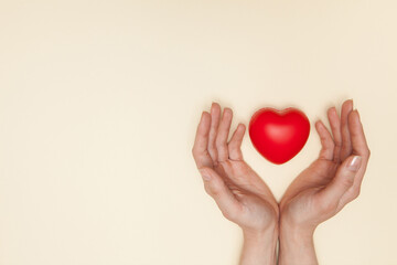 Health, medicine and charity concept - close up of female hands with small red heart.