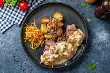 medallions of beef with creamy sauce and mushrooms on black plate top view