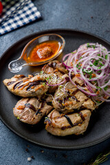 Kebab of pork with red onion and tomato sauce on black plate vertical