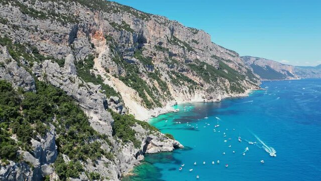 Baunei Coast, Cala Goloritze Beach and Tourist Boats at Turquoise Blue Sea in Sardinia, Italy - Aerial 4k
