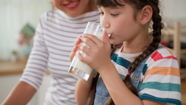 Caucasian little kid holding a cup of milk and drinking with mother.