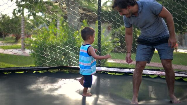 Young latin baby boy chasing his dad on a trampoline playing on a warm sunny summer afternoon